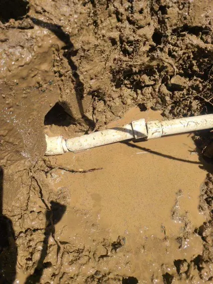 Cracked underground water line exposed and leaking in a muddy trench during leak detection in Hillsboro, Oregon