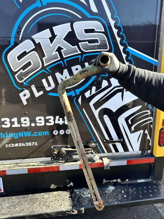 SKS Plumbing technician holding a badly corroded section of galvanized pipe beside the company service van in Hillsboro, Oregon