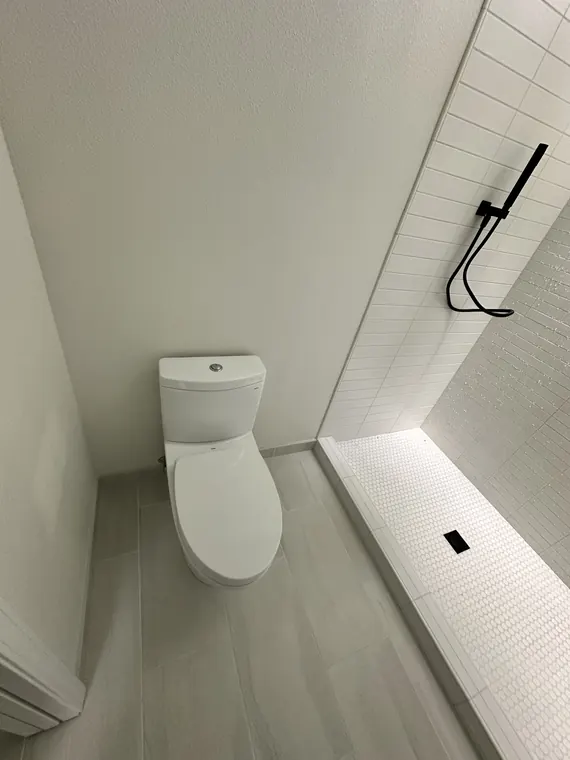 Remodeled bathroom with a new comfort-height toilet beside a curbless tiled shower with a linear drain in Hillsboro, Oregon
