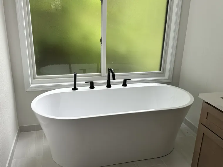 Freestanding white soaking tub with a matte black floor filler installed beneath a window in a Hillsboro, Oregon bathroom