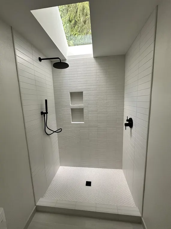 New rain shower head and handheld sprayer installed in a bright tiled shower with a skylight in Hillsboro, Oregon